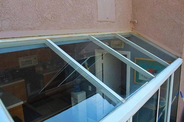 After: View from above of a glass ceiling or roof over a room, with angled glass panels freshly gleaming after window cleaning, and reflections of the interior, including framed pictures and furniture inside the room.