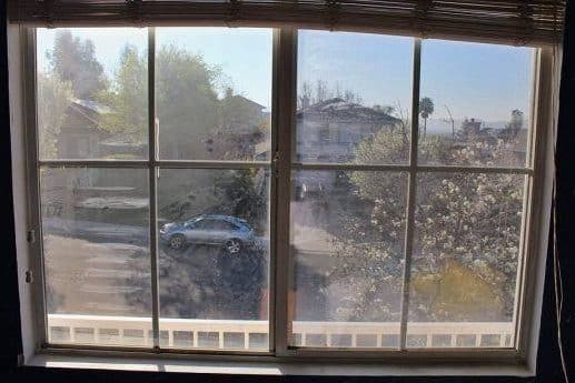 Before: A view through a bedroom window that is dirty and the glass appears cloudy, a street with cars and other homes are seen through the window.
