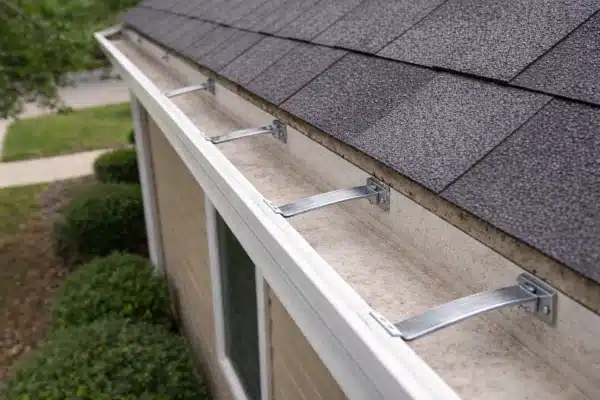 After: A roof gutter on a house showing a spotless gutter channel free of all debris after a gutter cleaning service. Asphalt shingle roofing above and green shrubs below are shown.