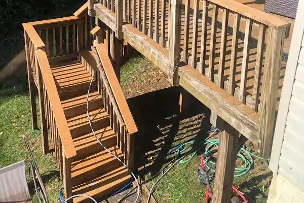 After: A wooden deck with stairs leading down to a grassy area, along with hoses and tools on the ground below.