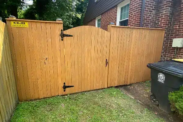 Before: A wooden fence gate with an arched top, flanked by two tall wooden panels, next to a trash bin on grass.