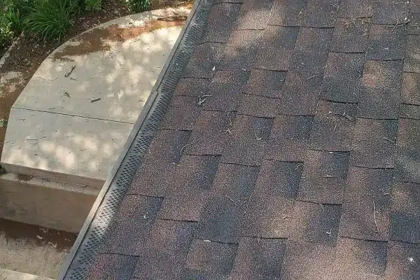 After: A close-up view of a roof with brown shingles and a section of a circular concrete walkway below.