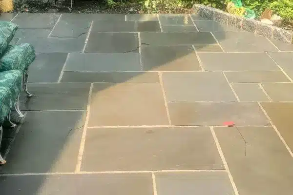 After: A stone patio with rectangular slate tiles, partially shaded, and green foliage in the background.