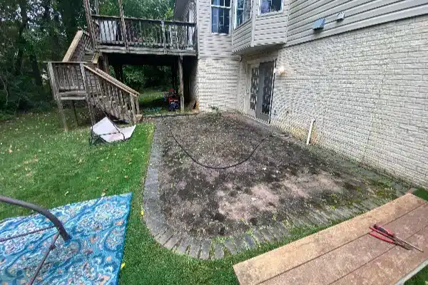 Before: Backyard with a partially paved area, grass, a blue rug, wooden deck, and a garden hose on the ground.